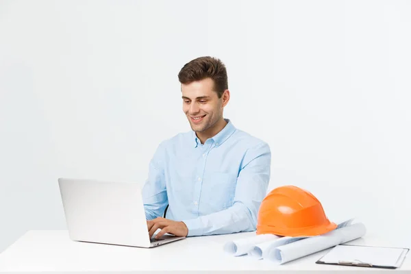 El apuesto ingeniero masculino está usando un cuaderno para trabajar. Él está sentado en el escritorio y sonriendo. Copiar espacio en el lado . — Foto de Stock