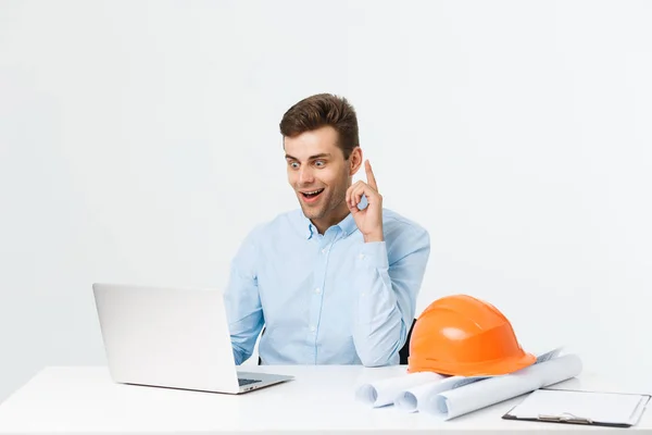 Der gut aussehende männliche Ingenieur arbeitet mit einem Notizbuch. Er sitzt am Schreibtisch und lächelt. Kopierraum auf der Seite. — Stockfoto