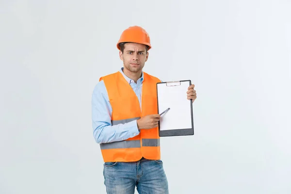Frustrado joven ingeniero con hardhat y chaleco reflectante comprobación de error en el documento sobre fondo gris — Foto de Stock
