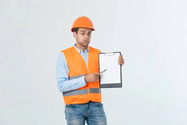 Frustrated young engineer with hardhat and reflective vest checking on mistake in document over gray background — Stock Photo, Image