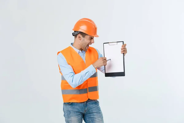Frustrated young engineer with hardhat and reflective vest checking on mistake in document over gray background — Stock Photo, Image