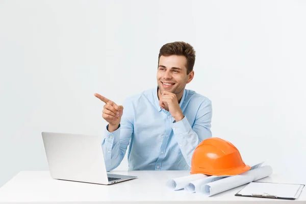 Porträt eines jungen männlichen Innenarchitekten oder Ingenieurs, der lächelnd auf seinem Bürotisch sitzt. — Stockfoto