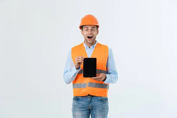 Shocked male engineer showing tablet screen, looks with opened mouth as remembers about important meeting. Male in stressful situation. Surprise and shock concept