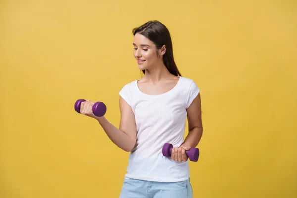 Shot of a beautiful and sporty young woman lifting up weights against yellow background. — Stock Photo, Image