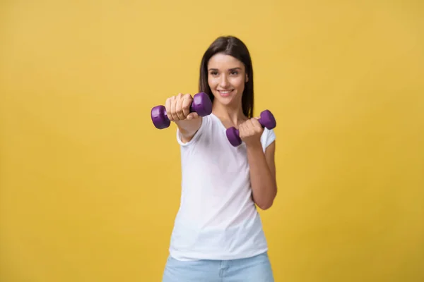 Shot of a beautiful and sporty young woman lifting up weights against yellow background. — Stock Photo, Image