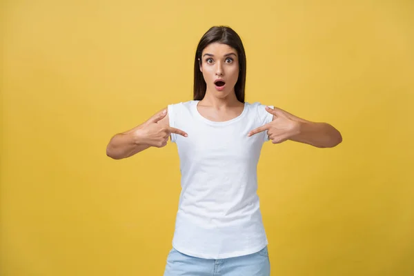 Amaze young woman pointing to one side with her finger while opening her mouth against a yellow background — Stock Photo, Image