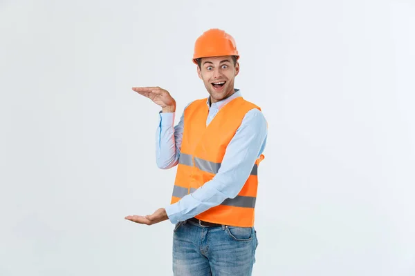 Joyeux ingénieur barbe tenant la main sur le côté et expliquant quelque chose, gars portant une chemise caro et un jean avec gilet jaune et casque orange, isolé sur fond blanc — Photo