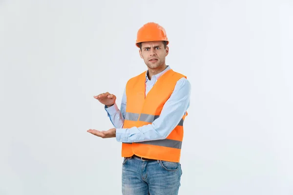 Joyeux ingénieur barbe tenant la main sur le côté et expliquant quelque chose, gars portant une chemise caro et un jean avec gilet jaune et casque orange, isolé sur fond blanc — Photo