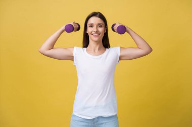 Sağlık ve Fitness kavramı: atış bir güzel ve sportif genç kadının sarı arka plana karşı ağırlık kaldırma.