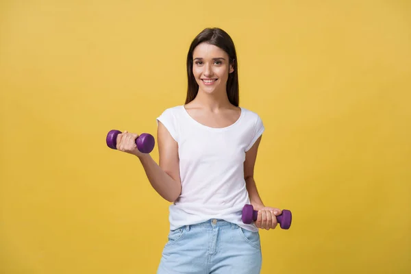 Health and Fitness Concept: Shot of a beautiful and sporty young woman lifting up weights against yellow background. — Stock Photo, Image