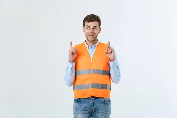 Beau jeune ingénieur homme sur le mur gris portant gilet orange étonné et surpris regardant et pointant avec les doigts . — Photo