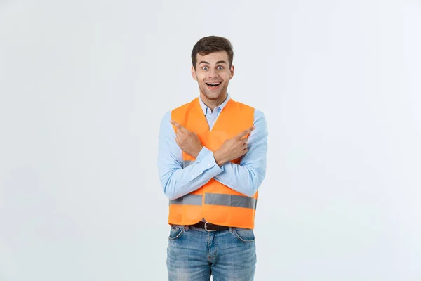 Bonito jovem engenheiro profissional homem sobre a parede cinza vestindo colete laranja espantado e surpreso olhando e apontando com os dedos . — Fotografia de Stock