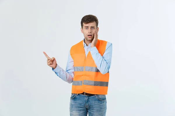 Stilig ung professionell ingenjör man över grå vägg klädd i orange väst förvånad och överraskad tittar och pekar med fingrar. — Stockfoto