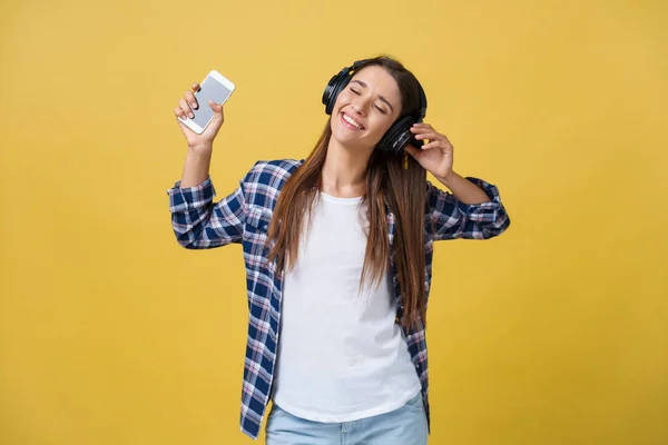 Lifestyle Concept - Portretul unei femei caucaziene frumoase, bucuroasă să asculte muzică pe telefonul mobil. Fundal galben pastel studio. Copiați spațiul . — Fotografie, imagine de stoc