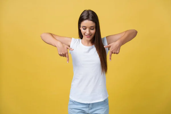 Happy young woman standing and pointing finger on copy space isolated over yellow gold wall background looking camera. — Stock Photo, Image