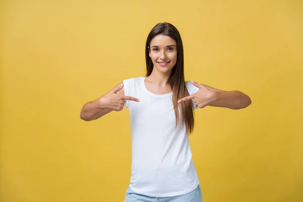 Mujer joven feliz de pie y apuntando con el dedo en el espacio de copia aislado sobre la pared de oro amarillo de fondo mirando cámara . —  Fotos de Stock