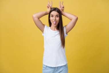 Eğlenceli ve insanlar kavramı - gülümseyen ve tavşan kulakları ile parmak üzerinde baş gösteren çiller ile mutlu beyaz bir kadın portresi Headshot. Pastel sarı stüdyo arka plan. Kopya alanı.