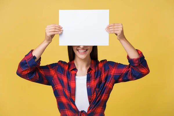 Smiling young woman holding white paper sheet. Studio portrait on yellow background. Stock Picture