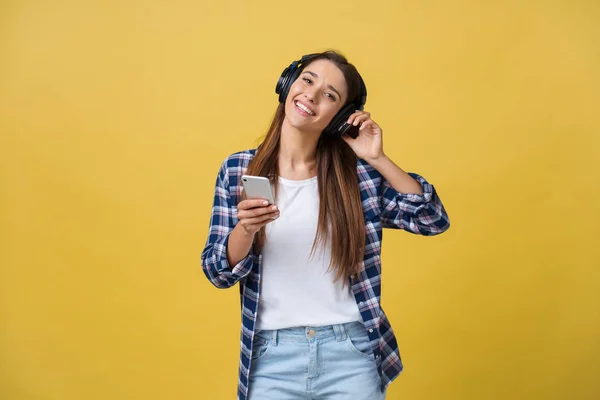 Belle jeune femme dans un casque écoutant de la musique et dansant sur fond jaune . — Photo