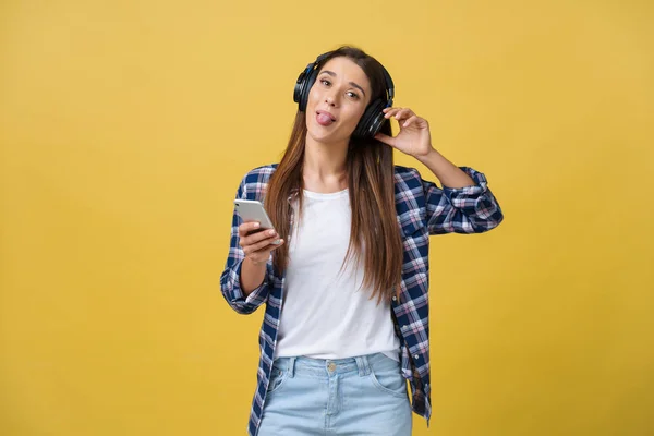 Belle jeune femme dans un casque écoutant de la musique et dansant sur fond jaune . — Photo