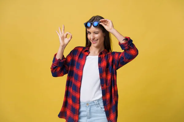 Retrato de uma menina feliz em roupas de verão mostrando gesto ok sobre fundo amarelo . — Fotografia de Stock