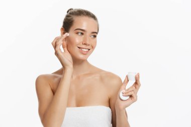 Yüzünde beyaz arka plan üzerinde izole kozmetik krem tedavisi uygulayarak güzel genç kadın