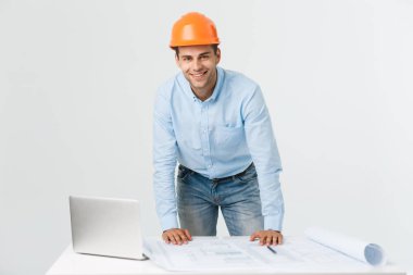 Onun yeni proje kendinden emin. ofisinde duran genç bir mühendis ve mimar adam üstünde laptop çalışma ve fotoğraf makinesi ile bakarak gülümsemek