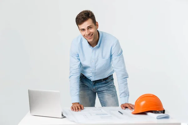 Vertrouwen in zijn nieuw project. jonge ingenieur en architect man die op laptop werkt en kijken naar de camera met glimlach terwijl staande op zijn kantoor — Stockfoto