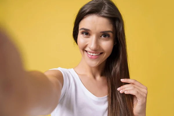 Selfie 스튜디오에 웃음 만드는 즐거운 매력적인 소녀. 밝은 노란색 배경에 자신의 사진을 복용 하는 갈색 머리와 함께 좋은 젊은 여자. — 스톡 사진