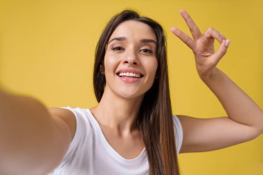 Güzel çekici kız selfie yapım stüdyosu ve gülüyor. Fotoğrafını parlak sarı zemin üzerine alarak kahverengi saçlı yakışıklı genç kadın.