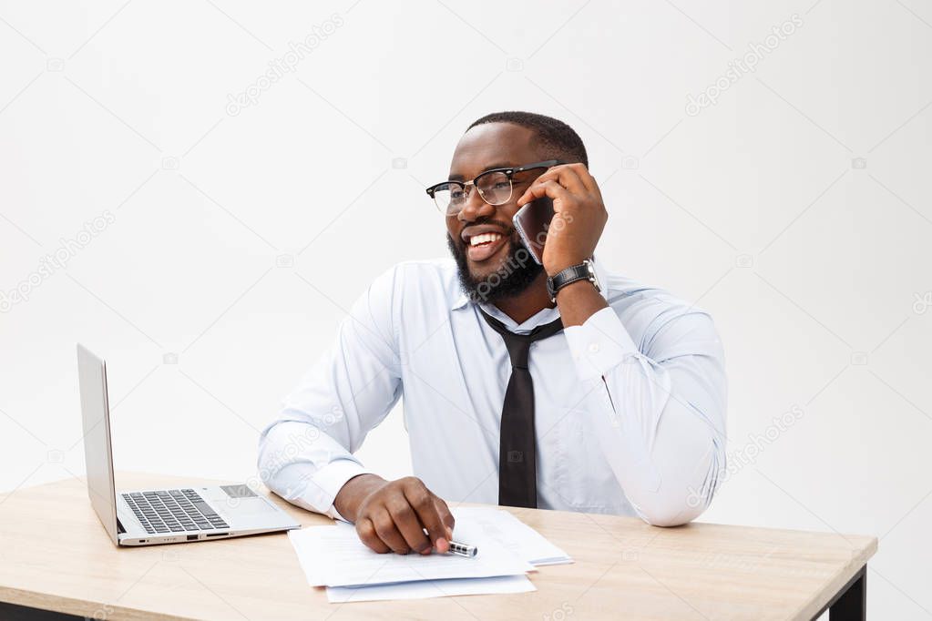 Cheerful and happy young dark-skinned businessman messaging online, checking newsfeed on social networks, using free wireless internet connection during break in modern office interior.