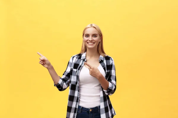 笑年轻的妇女在 t恤寻找和指向与拇指在黄色背景 — 图库照片