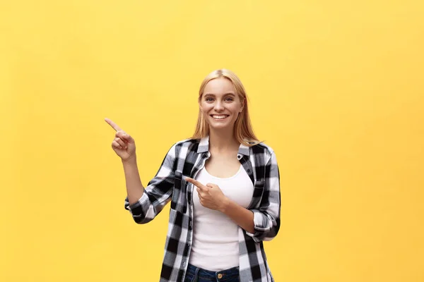 笑年轻的妇女在 t恤寻找和指向与拇指在黄色背景 — 图库照片