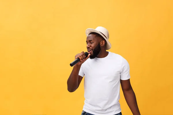 Молодий красивий афроамериканський хлопчик співає емоційно з мікрофоном ізольовано на жовтому фоні, в русі жестикулюючи — стокове фото