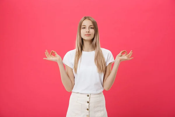 Blonde belle jeune femme fait signe mudra, se détend après une dure journée de travail, garde les yeux fermés, pratique le yoga sur fond rose. Jeune jolie femme médite à l'intérieur. Concept de détente . — Photo