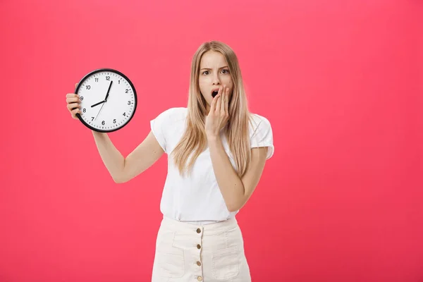 Amazed woman holding clock. Surprised woman in white t-shirt holds black clock. Retro style. Saving time concept. Summer sale. Discount. Isolated on pink background.
