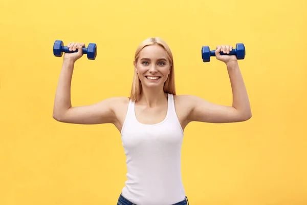 Fitness woman lifting weights smiling happy isolated on yellow background. Fit sporty Caucasian female fitness model. — Stock Photo, Image