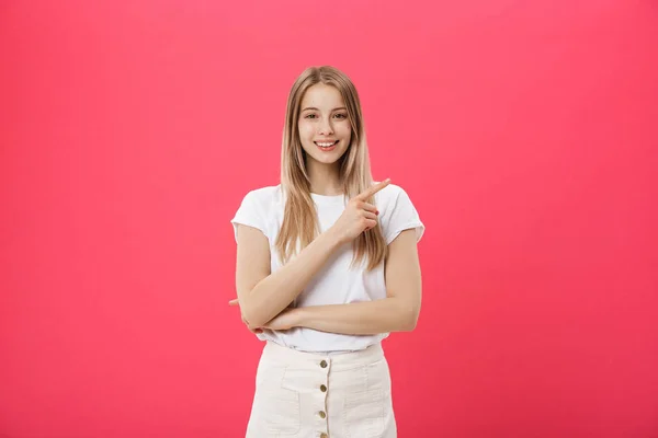 Милая молодая женщина в белой футболке указывает пальцем на изолированный розовый фон — стоковое фото