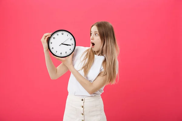 Amazed woman holding clock. Surprised woman in white t-shirt holds black clock. Retro style. Saving time concept. Summer sale. Discount. Isolated on pink background.