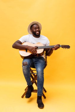 Tam uzunlukta fotoğraf heyecanlı sanatsal adam rahat süitte onun gitar çalmak. Sarı arka plan üzerinde izole.