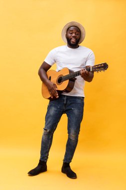 Tam uzunlukta fotoğraf heyecanlı sanatsal adam rahat süitte onun gitar çalmak. Sarı arka plan üzerinde izole.