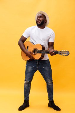 Tam uzunlukta fotoğraf heyecanlı sanatsal adam rahat süitte onun gitar çalmak. Sarı arka plan üzerinde izole.