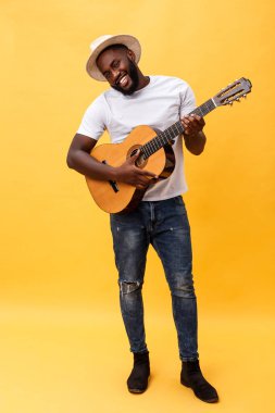 Tam uzunlukta fotoğraf heyecanlı sanatsal adam rahat süitte onun gitar çalmak. Sarı arka plan üzerinde izole.