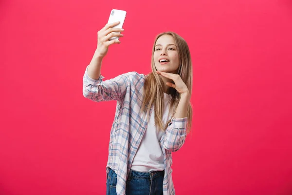 Очаровательная молодая женщина в белой шляпе путешествовать и сделать селфи на фронтальной камере смартфон позировать изолированы на сияющий розовый фон — стоковое фото