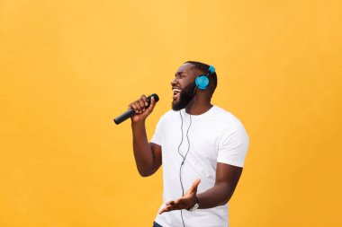 Holding mikrofon ve kulaklıklar üzerinde sarı arka plan izole hafta sonu tatil zevk kafa dinleme müzik şarkı şarkı üzerinde sahip neşeli pozitif şık yakışıklı Afrika adam portresi
