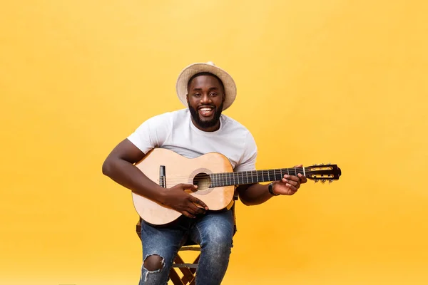 Homem negro musculoso tocando guitarra, vestindo jeans e blusa branca. Isolar sobre fundo amarelo . — Fotografia de Stock