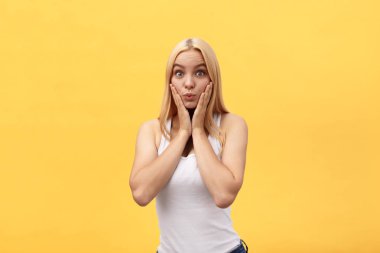 Sarı arka plan üzerinde izole kamera bakarken beyaz giysiler giyen sürpriz genç kadın.