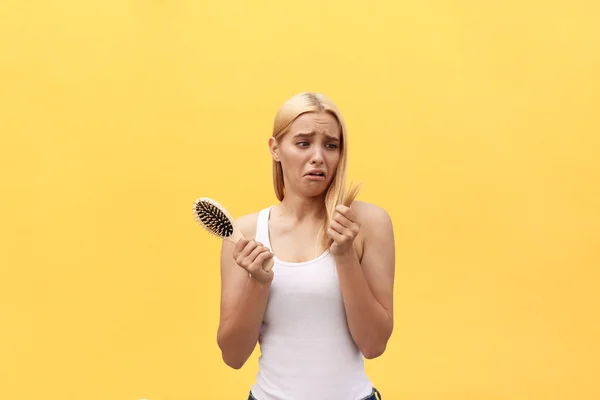 Sad girl looking at her damaged hair with comb in hand