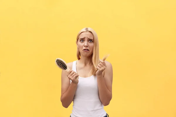 Sad girl looking at her damaged hair with comb in hand