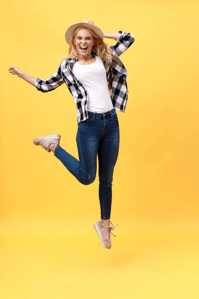 Portrait of surprised young woman in black pants jumping in front of yellow wall. Indoor portrait of young lady in fooling around in studio
